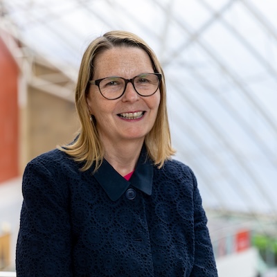 Headshot of Eileen Milner, a white woman with short blond hair, wearing round black glasses and navy blue top, smiling towards the camera.